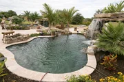 The completed pool area in the backyard of a property with a waterfall, garden and entertainment area.
