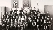 Ein Klassenportr&auml;t von jungen Schulkindern mit ihrem Lehrer vor einer Fotografie von Adolf Hitler und zwei Hakenkreuzen w&auml;hrend des Zweiten Weltkriegs, um 1940.