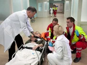 Rosie Pesch (Esther Esche, liegend) wird nach einem Blitzschlag von den Notärzten (Komparsen) in die Sachsenklinik eingeliefert. Als Dr. Kathrin Globisch (Andrea Kathrin Loewig, rechts) und Dr. Roland Heilmann (Thomas Rühmann, links) sie aufnehmen, bleibt ihr Herz stehen. Rosie muss reanimiert werden.