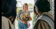 Franzi (Llewellyn Reichman, M.) überreicht den Eltern ihrer Freundin Blumen als Gast-Geschenk.