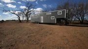 The white trim and grey siding is a beautiful pop of color against the field from the farm, for Ty and Taylor's build, in Enid, Oklahoma, as seen on Tiny House, Big Living.