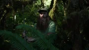 Matthew Raney in green t-shirt in forest holding his gun.