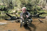 Jeremy Wade crouched in stream holding a giant freshwater crayfish with two hands out towards the camera. Jeremy Wade is behind the middle of the giant freshwater crayfish.