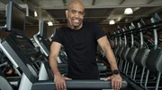 Marlow Williamson smiles for a picture as he places both hands on one side of the treadmill and slightly leans over.