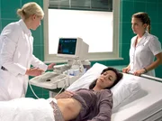 Dr. Isabel Dahl (Denise Zich, links) diagnostiziert einen Milzriss bei Aylin Demir (Suzan Demircan), der von einer seltenen Krankheit verursacht wird. Auch wenn Schwester Arzu Ritter (Arzu Bazman, rechts) skeptisch ist, veranlasst Isabel eine sofortige Operation.