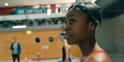 Ama (Amani-Jean Philippe) ist bei ihrem Schwimmwettbewerb und beobachtet einen Vogel unterm Dach der Schwimmhalle.