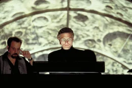 Der Verantwortliche der Truman Show ist Christof (Ed Harris, r.), Erfinder, Produzent und Regisseur. Alle Darsteller sind Schauspieler, nur der Star glaubt, am wirklichen Leben teilzunehmen ...