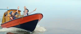 Pertsa (Olavi Kiiski) and Kilu (Oskari Mustikkaniemi) winken Kapit&auml;n Ritavuori (Veeti Kallio) aufgeregt von ihrem Boot aus zu.