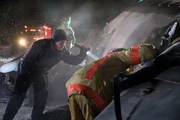 A rescuer (played by a background actor) shines a light into the crash site as a firefighter (played by a background actor) peers into the wreckage of Continental Airlines Flight 1713.