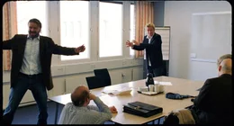 In den Verkaufsverhandlungen mit isl&auml;ndischen Interessenten l&auml;uft Kristoffer (Jens Albinus - rechts im Hintergrund) zu schauspielerischer Hochform auf, indem er Ravn (Peter Gantzler - links) regelrecht zum Hampelmann macht.
