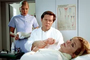 Dr. Stefan Frank (Sigmar Solbach) muss seiner Patientin Verena (Saskia Vester, liegend) mitteilen, dass sie Brustkrebs hat. Laura (Cecilia Kunz) verfolgt die beklemmende Situation.