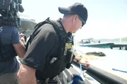 CBP AMO Agent Hud schaut über die Bordwand eines Bootes, während ein Kameramann hinter ihm in Fajardo, P.R. filmt (Lucky 8 TV/Paul Taggart).
