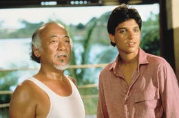 Mr. Miyagi (Pat Morita, l.) reist gemeinsam mit seinem Lehrling Daniel (Ralph Macchio) nach mehr als vier Jahrzehnten zur&uuml;ck in seine Heimat Okinawa. Dort wird er schon von seinem Erzfeind erwartet...