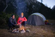 Checker Tobi (links) und Bergführer Simon Gietl wärmen sich vor ihrem Zelt am Lagerfeuer.
