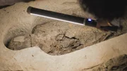 Professor Salima Ikram beleuchtet mit einem Lichtstab eine Mumie in einer 2 600 Jahre alten Grabanlage. Man kann bemalte Kartonnagen und Dutzende von Perlen erkennen, was darauf hindeutet, dass es sich um eine hochkar&auml;tige Bestattung handelt.