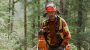 Brendan Bowman, a hand faller, stands near a tree with his chainsaw in Chamiss.