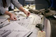 REENACTMENT - An investigator (played by a background performer) puts together the nuts and bolts found at the crash site and compares it to a diagram.