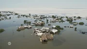 Luftaufnahme eines überfluteten Dorfes. Viele Häuser stehen teilweise unter Wasser, und nur die oberen Teile von Bäumen und Gebäuden sind sichtbar. Luftaufnahme eines überfluteten Dorfes. Viele Häuser stehen teilweise unter Wasser, und nur die oberen Teile von Bäumen und Gebäuden sind sichtbar.