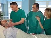 Herbert Stremann "Gurke" (Wofgang Häntsch, liegend) muss ein zweites Mal operiert werden, um ihm ein Karzinom zu entfernen. Als Dr. Roland Heilmann (Thomas Rühmann, links) und Dr. Kathrin Globisch (Andrea Kathrin Loewig, rechts) ihn um die Einwilligung bitten, wird "Gurke" plötzlich bewusstlos. Hans-Peter (Michael Trischan) soll Gaby Ludwig verständigen.