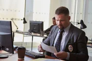 Detective Rodriguez sitzt an seinem Schreibtisch und sieht sich die Unterlagen der Polizeibehörde an.