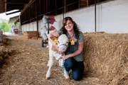 Veronika Kirchmaier sitzt im Stall und hält ein Kalb in den Armen.