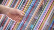 Worker adjusting multicoloured silk yarn on industrial loom in textile mill