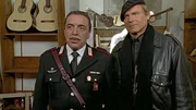 Maresciallo Cecchini und Don Matteo beobachten mit Neugier das Wiedersehen von Capitano Tommasi und seiner alten Freundin Chiara Brini. (Nino Frassica, Terence Hill, v.l.)