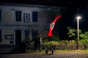 In einer nächtlichen Aktion zersägt der alte Heingeiger (Sigi Zimmerschied) mit Unterstützung anderer Dorfbewohner den Fahnenmast und verbrennt die Hakenkreuzfahne. In einer nächtlichen Aktion zersägt der alte Heingeiger (Sigi Zimmerschied) mit Unterstützung anderer Dorfbewohner den Fahnenmast und verbrennt die Hakenkreuzfahne.