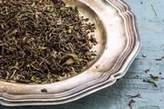 loser schwarzer Darjeeling-Tee auf einer Silberplatte auf rustikalem, blau lackiertem Holz, Nahaufnahme von oben loser schwarzer Darjeeling-Tee auf einer Silberplatte auf rustikalem, blau lackiertem Holz, Nahaufnahme von oben