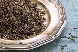 loser schwarzer Darjeeling-Tee auf einer Silberplatte auf rustikalem, blau lackiertem Holz, Nahaufnahme von oben