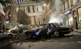 Die Attent&auml;ter haben die Stra&szlig;e zerst&ouml;rt und Autos durch die Luft fliegen lassen. Agent H (Chris Hemsworth) und Agent M (Tessa Thompson) haben mit ihren Waffen Deckung vor einem in der Stra&szlig;e liegenden Auto gesucht.