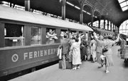 Ein typisches Produkt der "Wirtschaftswunderzeit" war der DER-Ferienexpress. Das Bild zeigt den Start des ersten Zuges am Frankfurter Hauptbahnhof als Deutschlands erster internationaler Rundreisezug zu einer Reise durch die L&auml;nder Schweiz, Italien und &Ouml;sterreich. In zw&ouml;lft&auml;giger Fahrt brachte der Express seine G&auml;ste nach Luzern, Lugano, Florenz, Rom, Neapel, Venedig und Innsbruck. Die auf Basis der Eilzugwagen f&uuml;r den DER-Ferienexpress aufgearbeiteten Sitzwagen C4(e)-36 boten nachts durch aufgespannte H&auml;ngematten den Urlaubern einen Liegeplatz in der 3. Klasse. Diese Z&uuml;ge waren die direkten Vorl&auml;ufer der modernen "TOUROPA"-Liegewagen-Urlaubsz&uuml;ge ab 1953. Der rechte Wagen - und vermutlich auch der n&auml;chste - ist ein sehr komfortabler DSG-Schlafwagen 1. und 2. Klasse der "Hecht"-Bauart WLAB-23.
