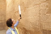 Prof. Salima Ikram benutzt einen Lichtstab, um Hieroglyphen an den W&auml;nden des Luxor-Tempels zu beleuchten. Obwohl der Besuch bei Tageslicht stattfindet, hilft der Lichtstab dabei, Licht und Schatten um die eingravierten Symbole herum zu manipulieren und erm&ouml;glicht ein leichteres Lesen des 3D-Textes.