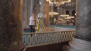 Dieses Bild zeigt eine Person, die ein modernes Vermessungsgerät auf einem Stativ im Inneren der Hagia Sophia bedient. Die Umgebung ist reich verziert mit großen Säulen, kunstvollen Kronleuchtern und historischen architektonischen Details, die auf die religiöse und kulturelle Bedeutung des Bauwerks hinweisen. Die Szene veranschaulicht den Einsatz zeitgenössischer Technologie zur Dokumentation und Analyse historischer Strukturen – ein zentrales Thema der Dokumentarserie über antike Superstrukturen. Dieses Bild zeigt eine Person, die ein modernes Vermessungsgerät auf einem Stativ im Inneren der Hagia Sophia bedient. Die Umgebung ist reich verziert mit großen Säulen, kunstvollen Kronleuchtern und historischen architektonischen Details, die auf die religiöse und kulturelle Bedeutung des Bauwerks hinweisen. Die Szene veranschaulicht den Einsatz zeitgenössischer Technologie zur Dokumentation und Analyse historischer Strukturen – ein zentrales Thema der Dokumentarserie über antike Superstrukturen.