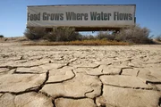 A sign on a farm trailer reading "Food grows where water flows," hangs over dry, cracked mud at the edge of a farm near Buttonwillow, California; Central Valley farmers and farm workers are suffering through the worsening California drought with extreme water shortages and job losses.