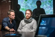 "SOKO Leipzig - Aus der H&ouml;lle": Jan Maybach (Marco Girnth) sitzt mit Bastian Drehwitz (Ole Fischer) im Vernehmungsraum der Kripo. Im Hintergrund sieht man eine an die Wand projizierte Karte und schwer bewaffnete Beamte, sowie im Vordergrund einen Tablet-PC auf dem Tisch und einen Monitor.