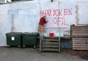 Signe (Wallis Grahn) entfernt an ihrer Hauswand Schmierereien, die ihren Sohn als Pädophilen denunzieren.