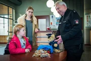 Wolle (Harald Maack, r.) ist froh, dass er der kleinen Lena (Malina Schächterle, l.), mit Hilfe seines Polizeibären, das von ihr sichergestellte Diebesgut entlocken konnte. Lenas Mutter Betti (Charlotte Puder, M.) versucht, noch einen Finderlohn für ihre Tochter rauszuschlagen.