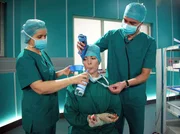 Dr. Elena Eichhorn (Cheryl Shepard, Mitte) verspürt während der Operation von Peter Merz ein krampfhaftes Ziehen im Unterleib. Dem Operationsteam (Komparsen) gibt Elena zu verstehen, dass es wohl nur ein kleiner Schwächeanfall nach einem schweren Tag war und dass es ihr schon wieder besser gehe.