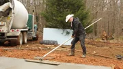 Marty is smoothing out concrete with a large tool that resembles a mop.
