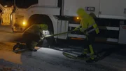Thord bekommt Hilfe vom Fahrer eines Lastwagens, um einen Riemen am Vorderrad eines Lieferwagens zu befestigen.