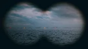 Through binoculars boats in a line on the horizon on fire. Through binoculars boats in a line on the horizon on fire.