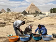 Dr. Claire Malleson untersucht die Trümmer des neu entdeckten königlichen Gebäudes in der Stadt der Pyramidenbauer, mit der Großen Pyramide im Hintergrund auf dem Gizeh-Plateau, Kairo, Ägypten.