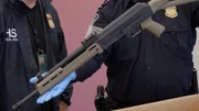 Ein CBP-Beamter h&auml;lt eine Schusswaffe in der Hand, die bei einer Lieferung von Lautsprechern beschlagnahmt wurde. (National Geographic)