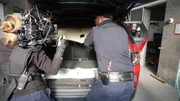 Ein CBP-Beamter arbeitet an der Grenze von San Ysidro daran, Pakete mit mutma&szlig;lichen Bet&auml;ubungsmitteln aus dem Fahrzeug eines Verd&auml;chtigen zu bergen, w&auml;hrend ein Kameramann filmt.