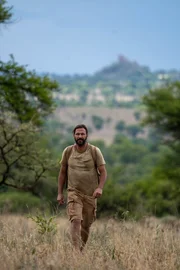 Hazen wandert durch das Gestr&uuml;pp mit der Serengeti im R&uuml;cken.