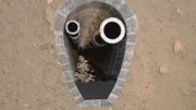 Das Bild zeigt einen tiefen, sich verjüngenden Schacht, der mit Steinblöcken ausgekleidet ist, mit zwei großen metallischen Rohrelementen, die sich vertikal ins Innere erstrecken. Das Bild zeigt einen tiefen, sich verjüngenden Schacht, der mit Steinblöcken ausgekleidet ist, mit zwei großen metallischen Rohrelementen, die sich vertikal ins Innere erstrecken.