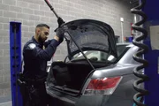 CBP-Beamter Elizondo hebt mit einer Metallstange die Innenverkleidung des Kofferraums eines Verd&auml;chtigen auf, um nach geschmuggelten Drogen zu suchen (National Geographic for Disney).