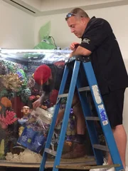 Wayde stands on a ladder watching as Kyle inserts sand into the tank.