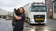 Ep9 - Louise twisted to her left to the camera, in front of her truck holding her dog, truck to the right of the frame, smiling